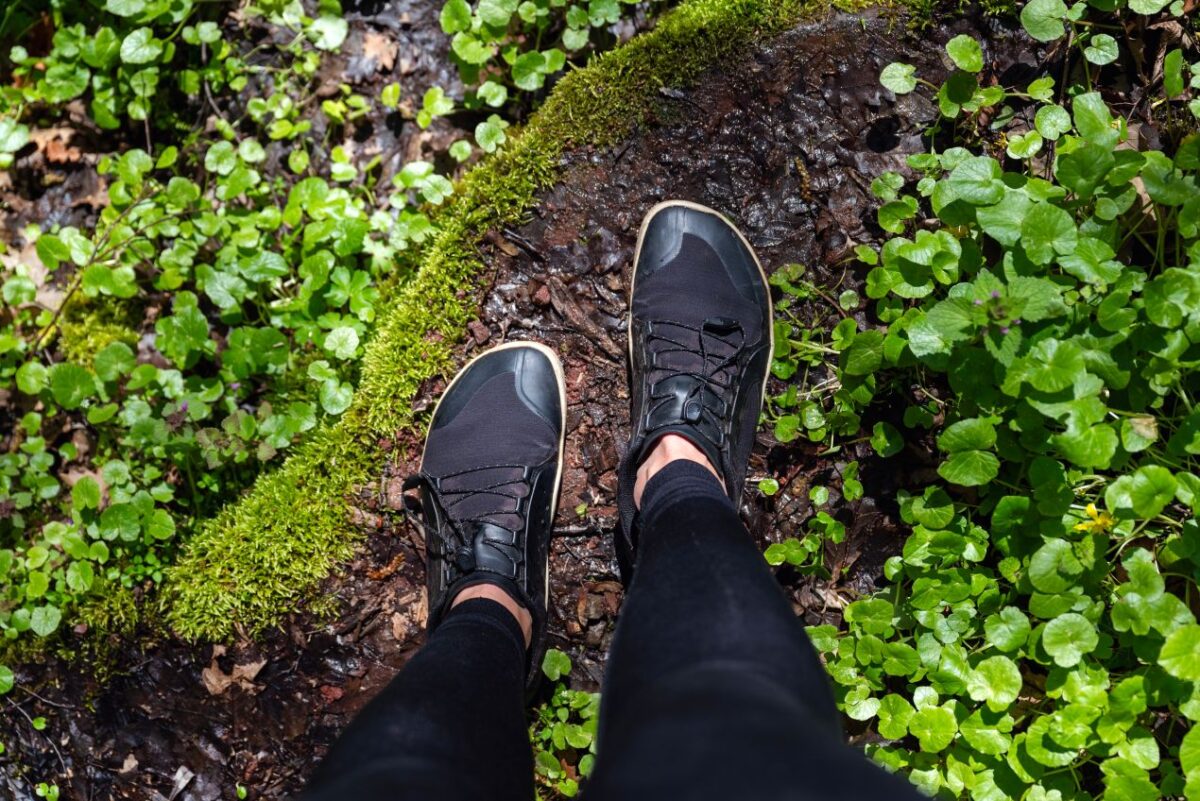 Person mit Barfussschuhen geht durch feuchten Waldboden – natuerliches Gehgefuehl und direkter Kontakt zur Umwelt mit Barfussschuhen erleben